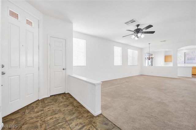 empty room with ceiling fan with notable chandelier and dark colored carpet