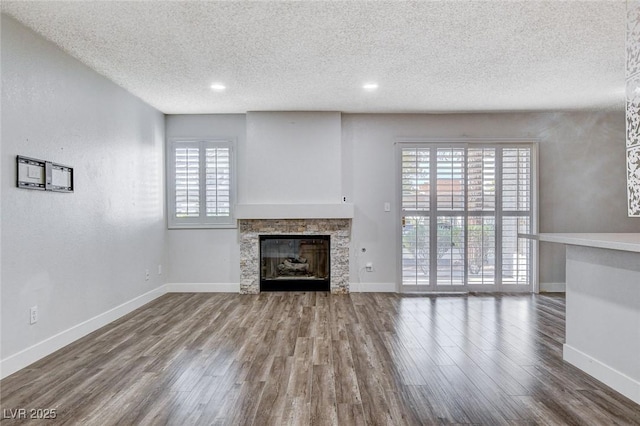 unfurnished living room with a fireplace, a textured ceiling, hardwood / wood-style flooring, and a wealth of natural light