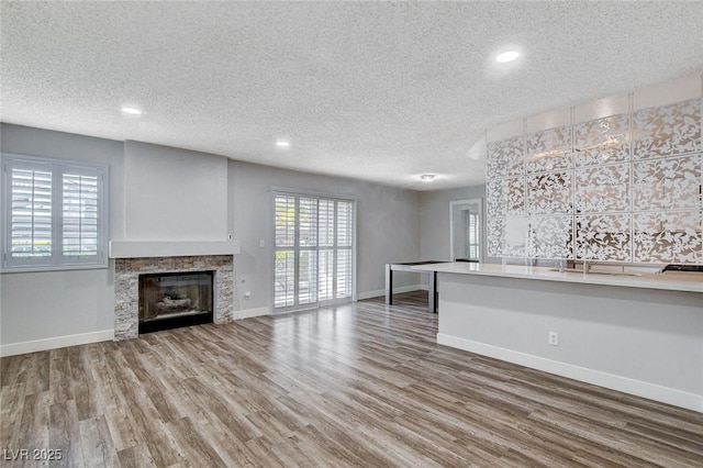 unfurnished living room featuring a stone fireplace, a textured ceiling, and hardwood / wood-style flooring