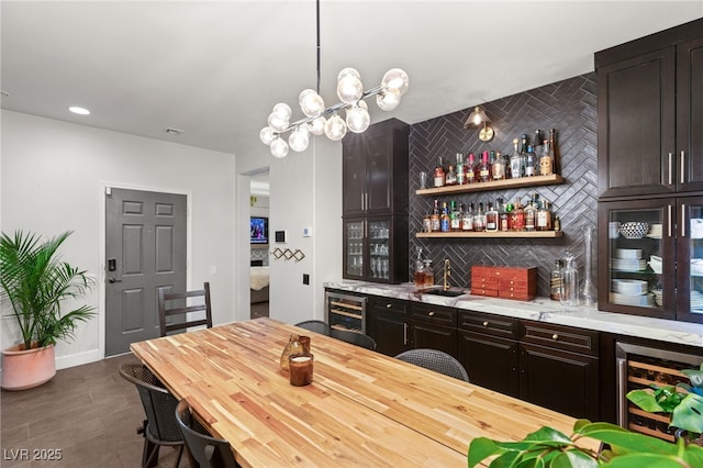 bar featuring dark brown cabinets, backsplash, wine cooler, and hanging light fixtures