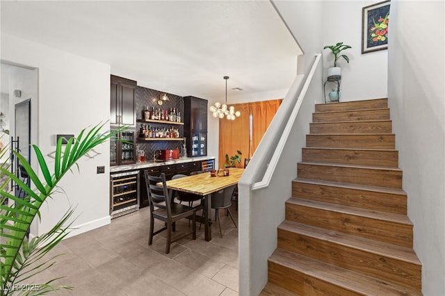 bar featuring dark brown cabinets, sink, wood walls, an inviting chandelier, and beverage cooler