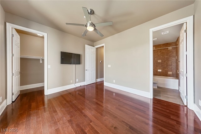 unfurnished bedroom with ceiling fan, a spacious closet, ensuite bathroom, a closet, and hardwood / wood-style flooring