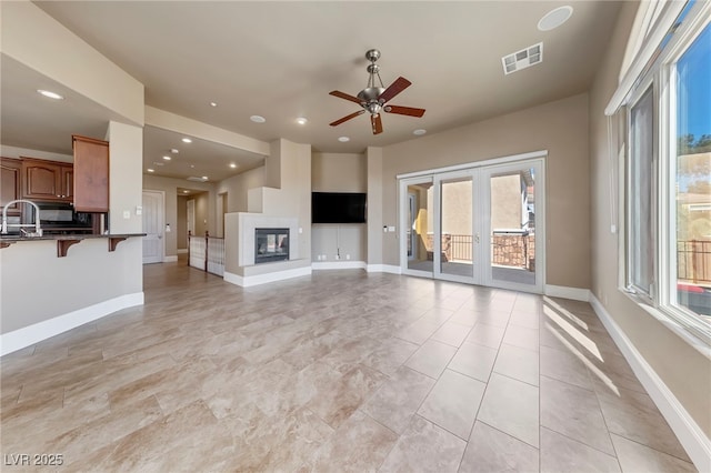 unfurnished living room with a multi sided fireplace, french doors, and ceiling fan