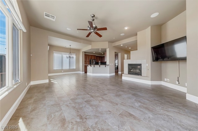 unfurnished living room featuring a tiled fireplace and ceiling fan with notable chandelier