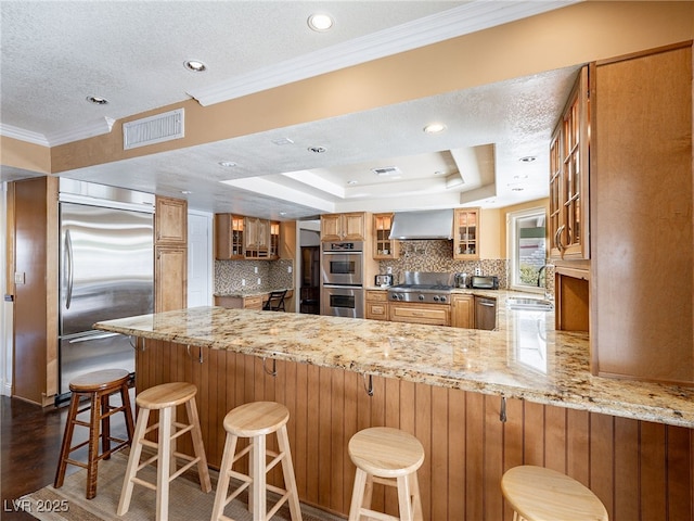 kitchen with kitchen peninsula, ventilation hood, stainless steel appliances, and a kitchen breakfast bar