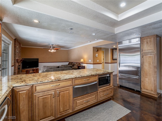 kitchen with light stone countertops, ceiling fan, built in appliances, a textured ceiling, and a tray ceiling