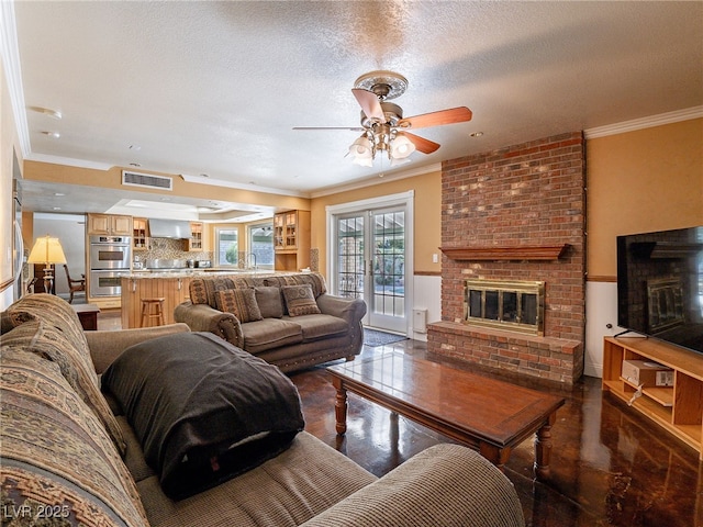 living room featuring a textured ceiling, ceiling fan, ornamental molding, and a fireplace