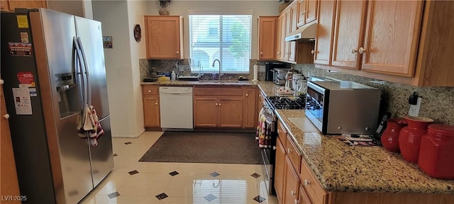 kitchen with appliances with stainless steel finishes, backsplash, light stone counters, and sink