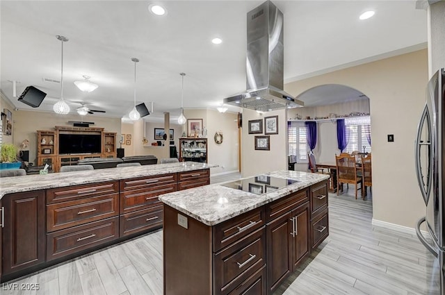 kitchen featuring stainless steel fridge, black electric stovetop, island range hood, a center island, and hanging light fixtures