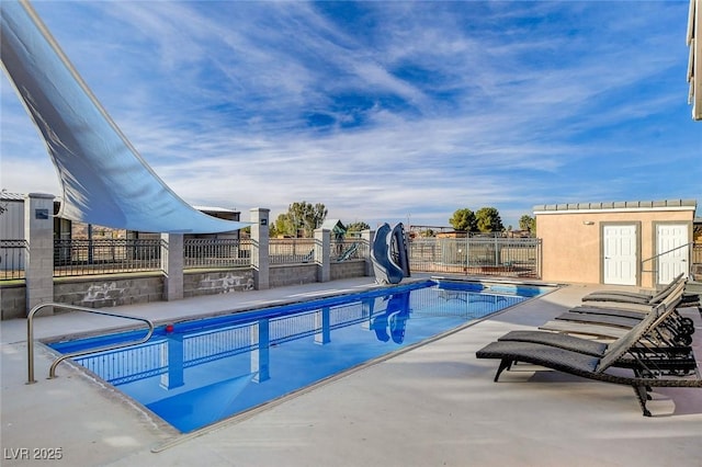 view of swimming pool featuring an outbuilding, a water slide, and a patio