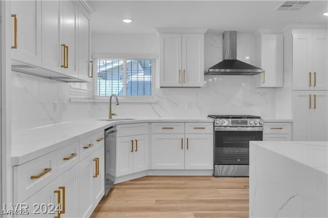 kitchen featuring white cabinetry, sink, wall chimney range hood, light stone counters, and appliances with stainless steel finishes