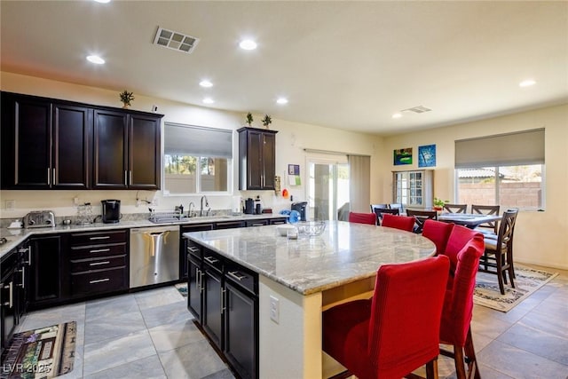 kitchen featuring a breakfast bar, a center island, sink, stainless steel dishwasher, and light stone countertops