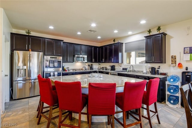 kitchen featuring light stone countertops, a center island, sink, a kitchen breakfast bar, and appliances with stainless steel finishes