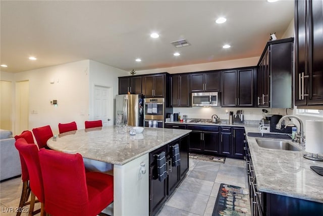 kitchen featuring light stone counters, a breakfast bar, stainless steel appliances, sink, and a center island