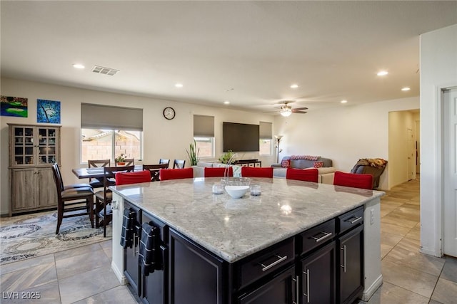 kitchen with ceiling fan, a kitchen island, light tile patterned flooring, and light stone countertops