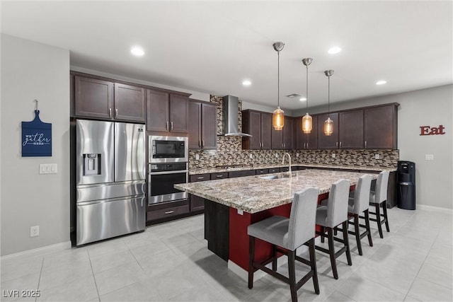 kitchen featuring wall chimney exhaust hood, stainless steel appliances, a kitchen island with sink, sink, and decorative light fixtures