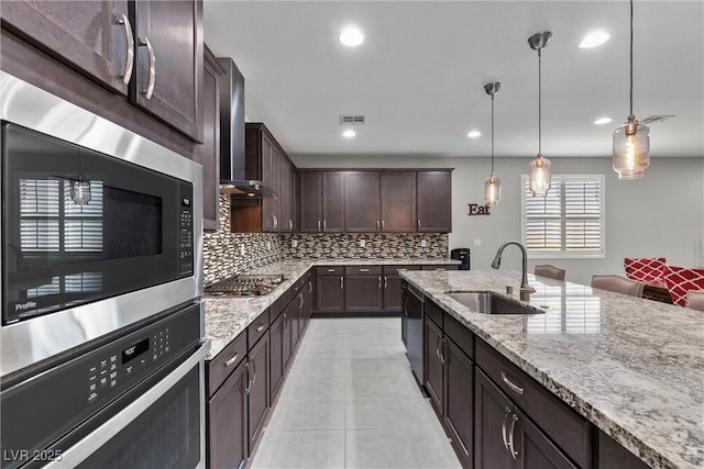 kitchen with dark brown cabinetry, sink, wall chimney range hood, decorative light fixtures, and appliances with stainless steel finishes