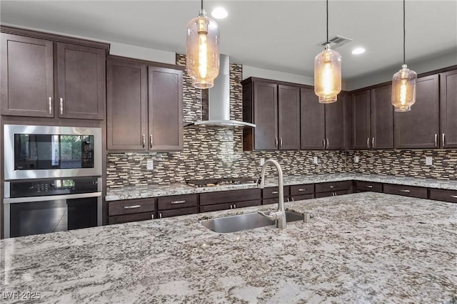 kitchen featuring wall chimney range hood, dark brown cabinetry, hanging light fixtures, and sink