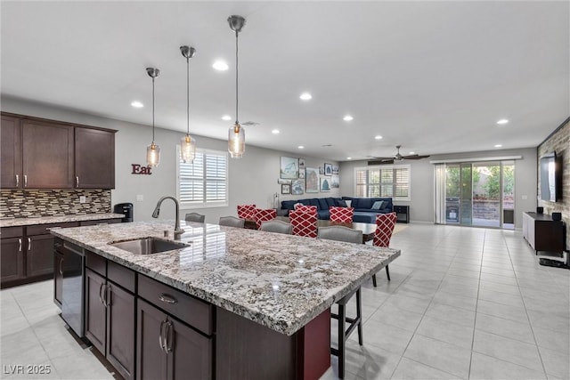 kitchen with ceiling fan, sink, hanging light fixtures, a kitchen island with sink, and decorative backsplash