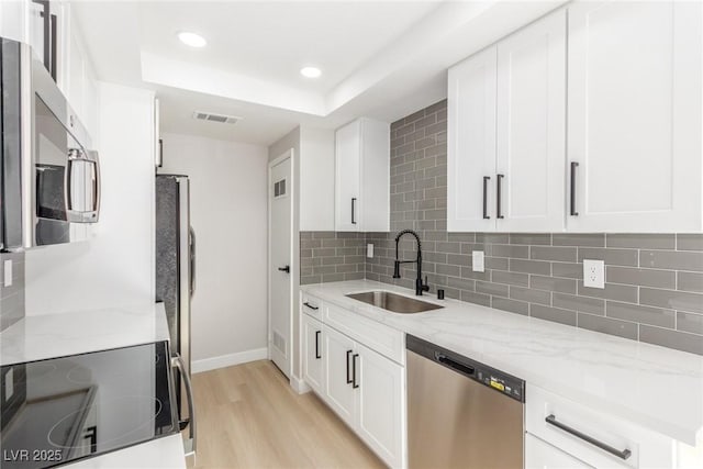 kitchen featuring appliances with stainless steel finishes, light stone counters, a raised ceiling, and sink