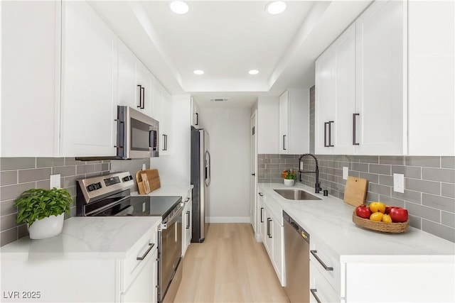 kitchen featuring tasteful backsplash, stainless steel appliances, a tray ceiling, sink, and white cabinets