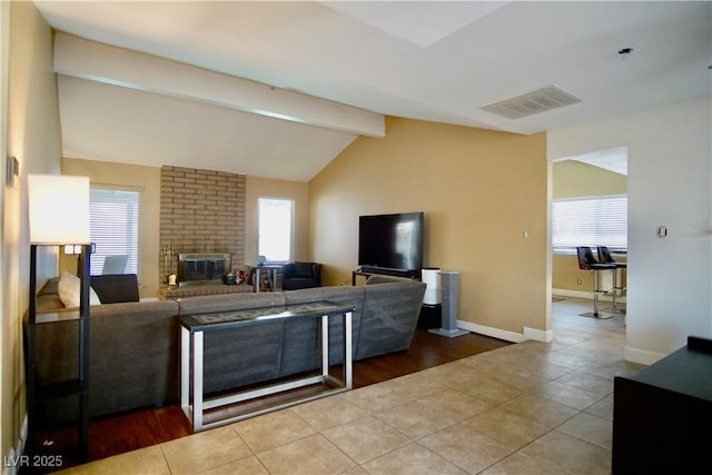 tiled living room featuring lofted ceiling with beams, a brick fireplace, and a wealth of natural light