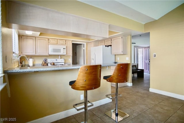 kitchen featuring sink, a breakfast bar area, dark tile patterned floors, kitchen peninsula, and white appliances