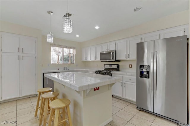 kitchen featuring appliances with stainless steel finishes, pendant lighting, a center island, white cabinetry, and tile counters