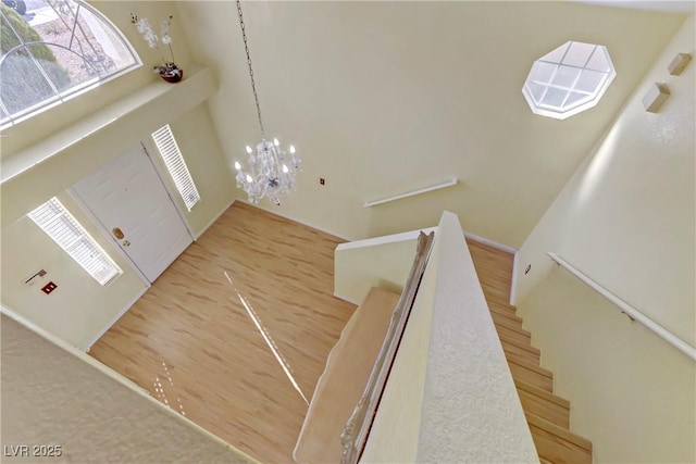 staircase with a towering ceiling, wood-type flooring, and an inviting chandelier