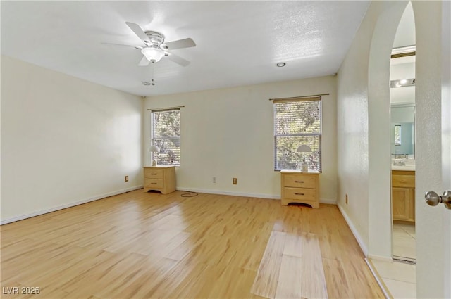 unfurnished bedroom featuring multiple windows, ensuite bathroom, ceiling fan, and light hardwood / wood-style floors