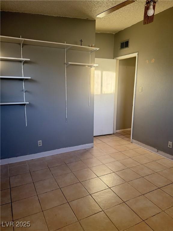 unfurnished bedroom with ceiling fan, a closet, light tile patterned floors, and a textured ceiling