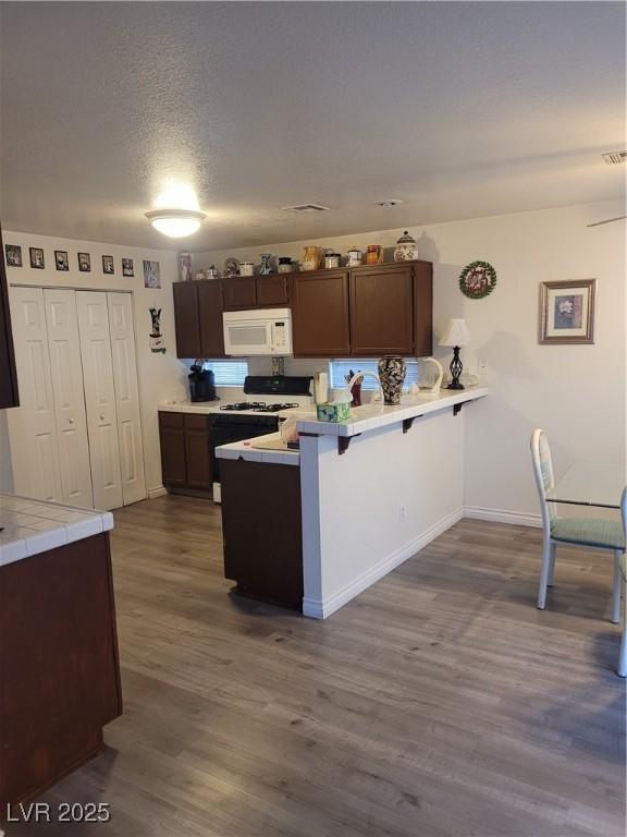 kitchen featuring gas stove, dark brown cabinets, a kitchen breakfast bar, and kitchen peninsula