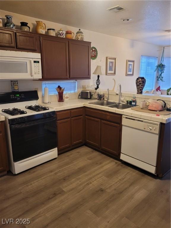 kitchen featuring dark brown cabinetry, sink, tile counters, dark hardwood / wood-style floors, and white appliances