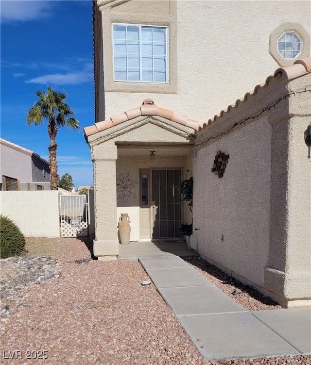 entrance to property featuring a tiled roof, fence, and stucco siding