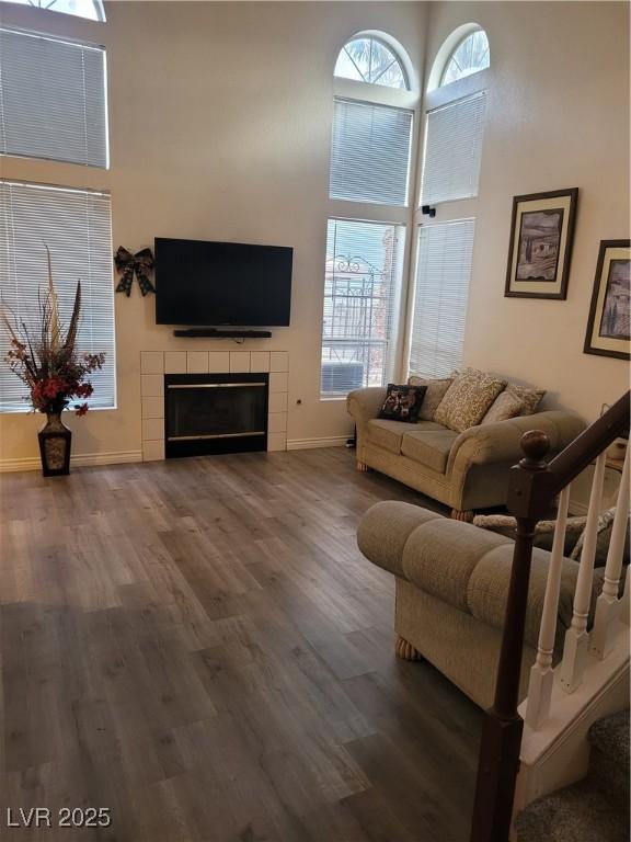 living room featuring hardwood / wood-style flooring, a towering ceiling, and a tile fireplace