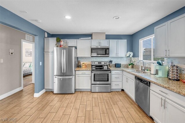 kitchen with white cabinets, sink, decorative backsplash, light stone countertops, and appliances with stainless steel finishes