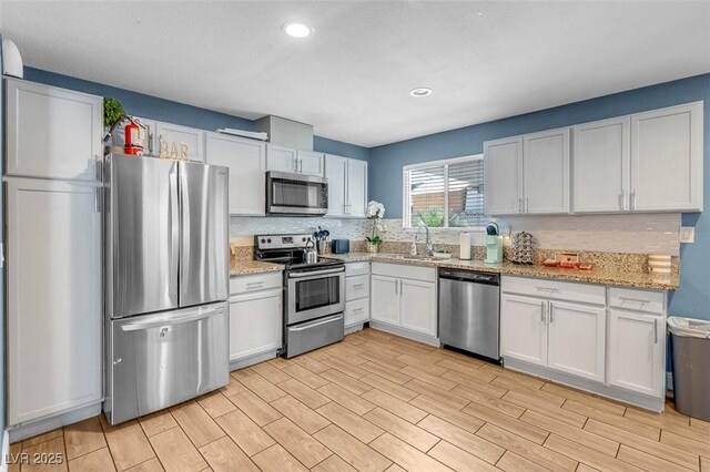 kitchen with sink, appliances with stainless steel finishes, tasteful backsplash, light stone counters, and white cabinetry