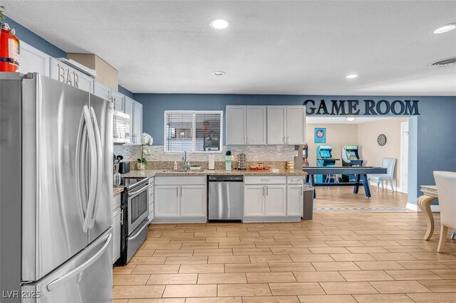 kitchen featuring backsplash, white cabinets, sink, light stone countertops, and stainless steel appliances