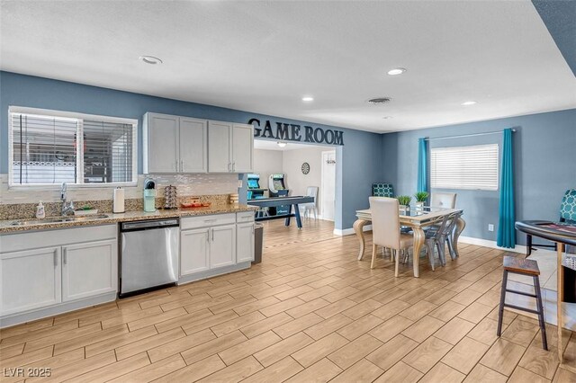 kitchen featuring sink, light stone counters, stainless steel dishwasher, decorative backsplash, and white cabinets