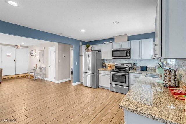 kitchen with sink, stainless steel appliances, light stone counters, light hardwood / wood-style flooring, and backsplash