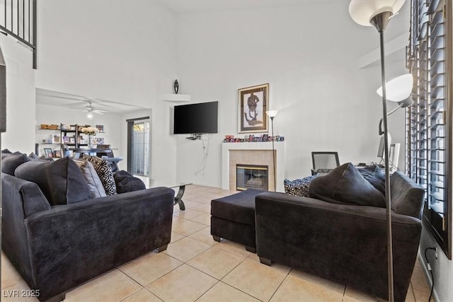 living room with ceiling fan, a towering ceiling, light tile patterned floors, and a tiled fireplace