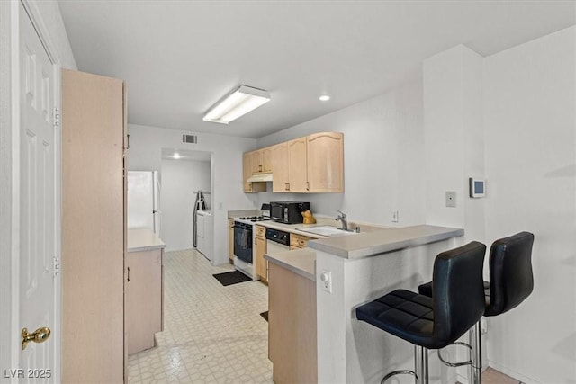 kitchen featuring kitchen peninsula, light brown cabinetry, a kitchen breakfast bar, white appliances, and washing machine and clothes dryer