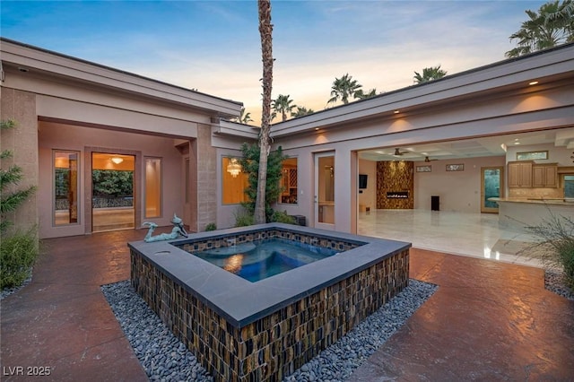 pool at dusk featuring an in ground hot tub and a patio