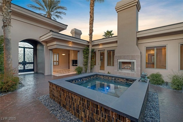 pool at dusk featuring an in ground hot tub, a patio area, and a tiled fireplace