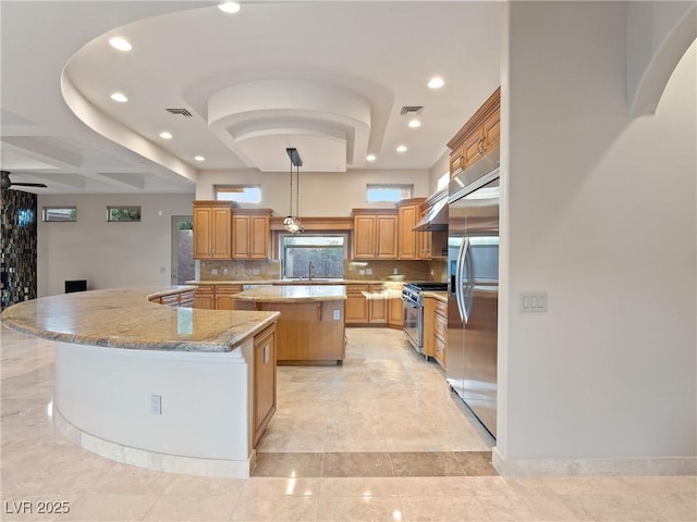 kitchen featuring light stone countertops, sink, premium appliances, backsplash, and a kitchen island