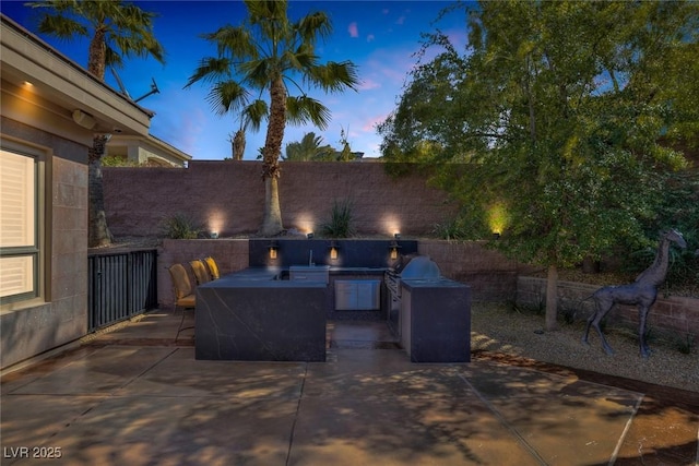 patio terrace at dusk featuring area for grilling and an outdoor kitchen