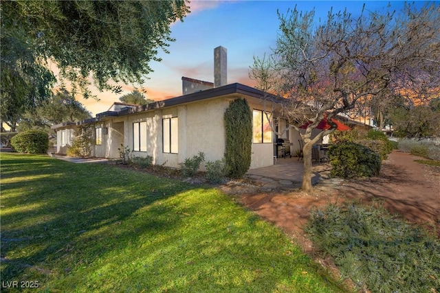 property exterior at dusk with a patio area and a lawn