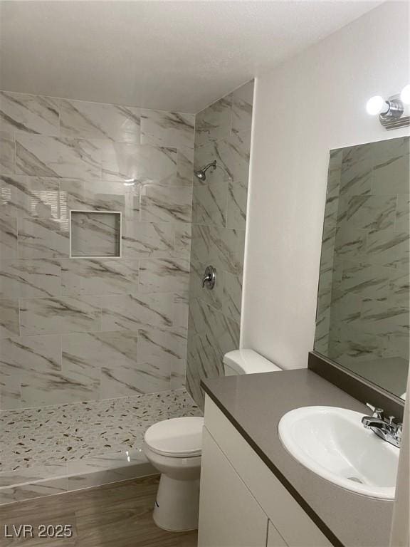 bathroom featuring hardwood / wood-style flooring, toilet, vanity, and tiled shower