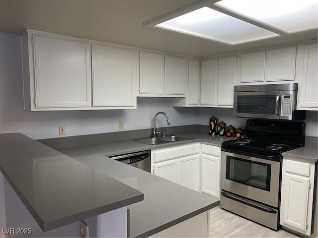 kitchen with kitchen peninsula, white cabinetry, sink, and appliances with stainless steel finishes