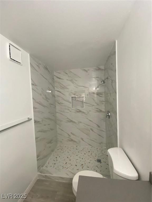 bathroom featuring a tile shower, hardwood / wood-style flooring, and toilet